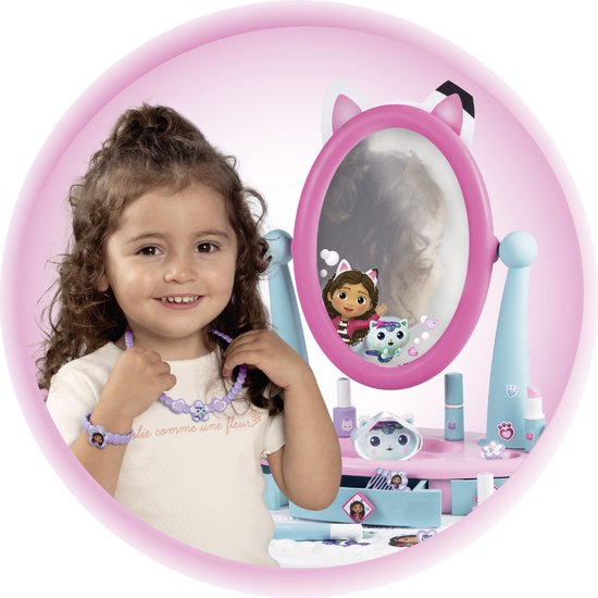 Meisje met krullend haar met ketting draagt een paarse armband en staat bij de Gabby's Dollhouse kaptafel.
