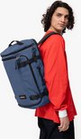 Man met krullend haar draagt een donkerblauwe Eastpak reistas op zijn rug.