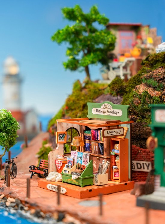 Miniatuur boekenwinkel "The Muse Bookshop" model in een buitenomgeving met vuurtoren en zee.