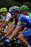 Wielrenners in blauw-witte, witte en groene tenues, dragen helmen en zonnebrillen.