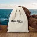Pochette en velours blanc cassé avec le logo Malinsi Jewelry, près d'un morceau de bois flotté.