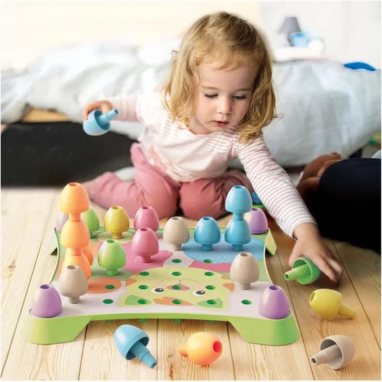 Meisje speelt met paars, geel, groen en oranje peg-art knoppen op een groen pegboard met giraffenafbeelding.