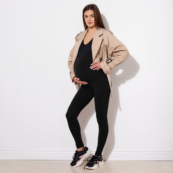 Zwangerschapslegging in het zwart met een beige trenchcoat, gedragen door een model