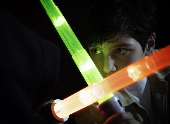 Garçon avec des sabres laser verts et rouges dans un environnement sombre.