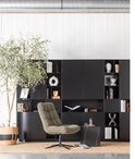 Zwarte boekenkast met diverse open en gesloten vakken, een groene fauteuil en een grote groene plant.