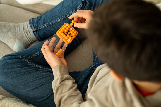 Jongen met spijkerbroek en grijze sokken speelt met een oranje IQ Mini spel.