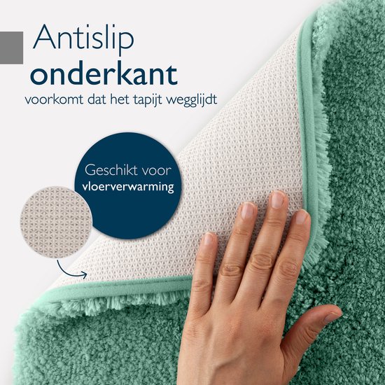 Hand toont de antislip onderkant van een groene badmat. Geschikt voor vloerverwarming.