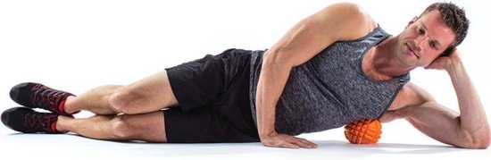 Man ligt op zijn zij met oranje massagebal onder zijn heup.