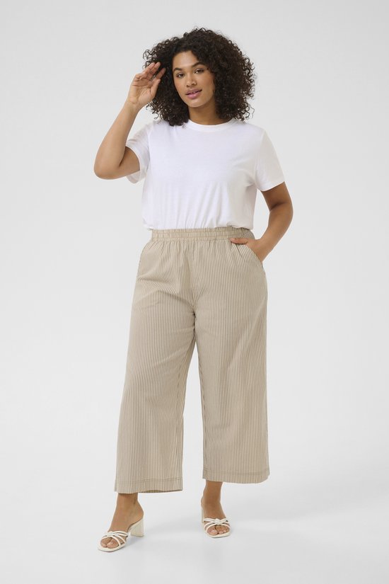Model met krullend haar, in wit T-shirt en beige gestreepte broek.