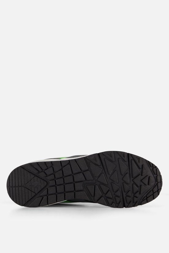Onderkant van grijze sneaker met zwart loopvlak en neon groene accenten.