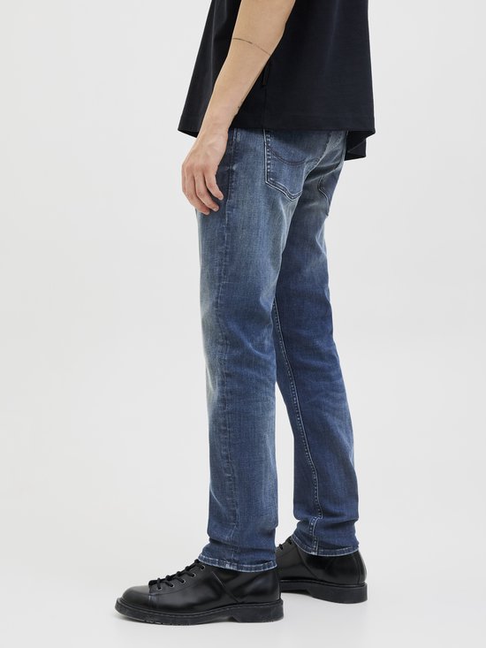 Zijaanzicht van de benen van een man in een zwart T-shirt en blauwe jeans.