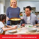 Familie aan tafel, moeder draagt een zwarte multicooker met pasta. De kookfunctie maakt pasta maken gemakkelijk.