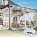 Transparante zeildoekwanden die een moderne pergola met buitenmeubilair afsluiten, met zicht op een tuin. Gevouwen zeildoek in de hoek.