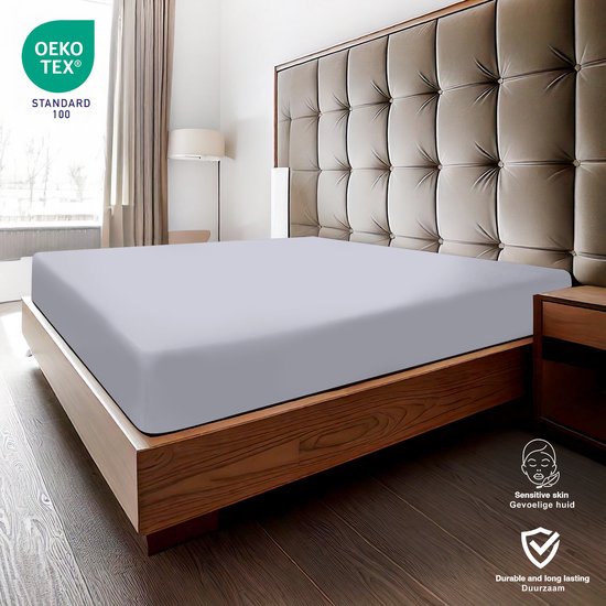 Drap plat gris sur un lit avec tête de lit capitonnée, doux pour peaux sensibles.