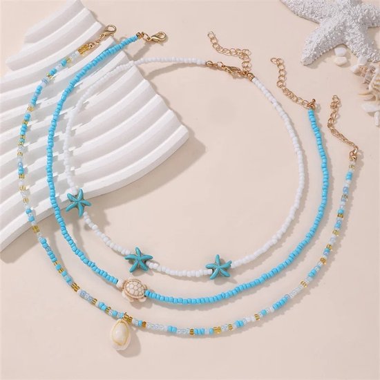 Drielaagse ketting met blauwe, witte en gouden kralen, versierd met turkoois gekleurde zeesterren, een schildpad en een schelp.