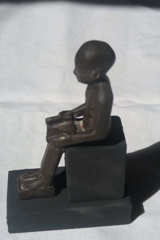 Bruin beeldje van een bukkende figuur, op een zwarte sokkel.