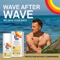 Een man met een gebruinde huid in zee, met een fles P20 Original SPF 30 zonnebrandspray.