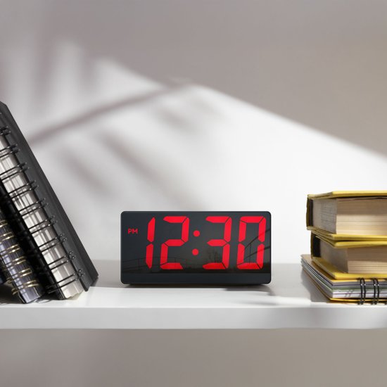 Digitale wekker met rood display dat 12:30 weergeeft, op een plank.