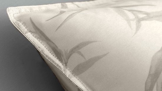 Een detail van een kussensloop met een licht beige kleur en een grijs patroon van bladeren.