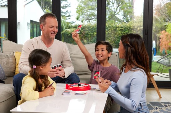 Familie speelt UNO Spin spel in woonkamer, met rode spinwiel en kaarten op tafel.