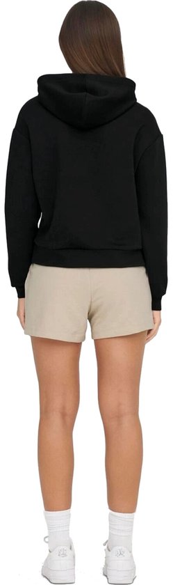 Model draagt een zwarte cropped hoodie en beige shorts, van achteren gezien.