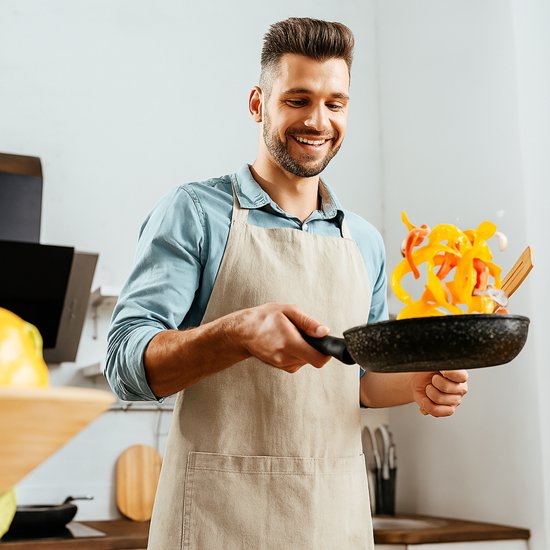 Man met schort die paprika's bakt in een zwarte koekenpan met granieten look.