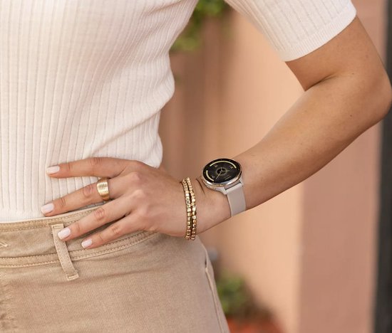 Vrouw met een lichtbruine smartwatch, gouden armbanden en ring.