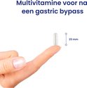 Een multivitamine capsule op een vingertop, met naast de capsule een maatstreep van 23 mm.