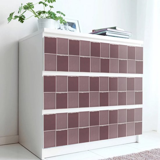 Commode blanche ornée de carreaux carrés violet lilas sur les façades des tiroirs, avec une plante posée dessus.