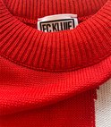 Label met 'FC Kluif' op de kraag van een rode gebreide trui.