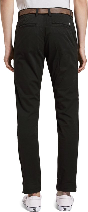 Model draagt een zwarte chino, van achteren gezien, met een bruine riem en witte sneakers.