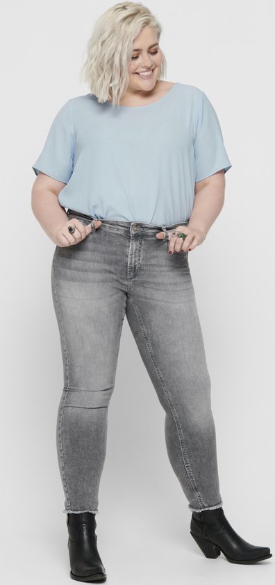 Model met blond haar in een lichtblauwe top en grijze skinny jeans met rafelige zoom.