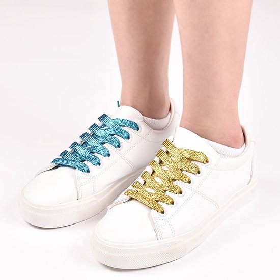 Kind met witte sneakers, één schoen met turquoise glitterveters, de ander met goudkleurige glitterveters.
