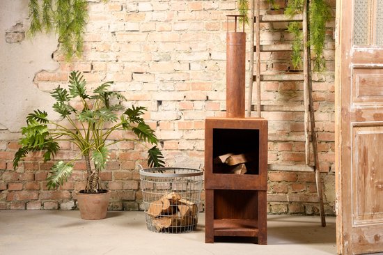 Roestkleurige buitenkachel met schoorsteen, vol met houtblokken, naast een plant en mand met hout.