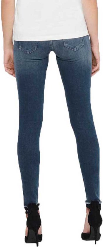Achterkant van model met blauwe skinny jeans met raw-edge enkelbroekspijpen en zwarte hakken.
