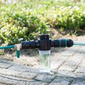 Waterfilter met groene slang en zwarte aansluitingen, op een stenen ondergrond.