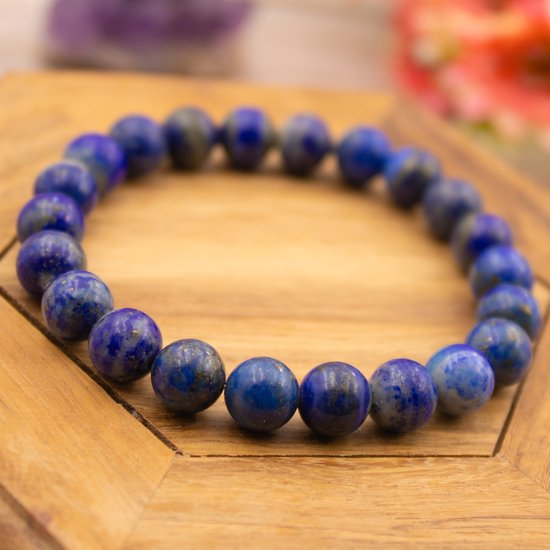 Armband van lapis lazuli kralen in verschillende blauwtinten met gouden spikkels, op een houten ondergrond.