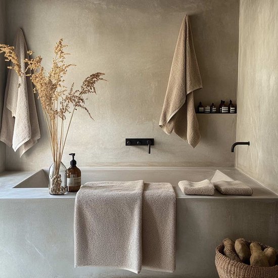 Stijlvolle badkamer met beige badtextiel, houten mand en droogbloemen in een glazen vaas bij een badkuip.