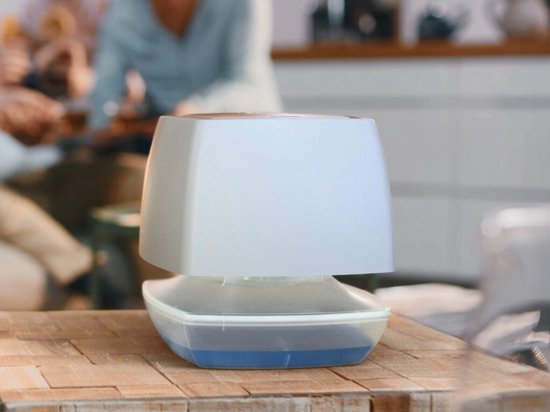 Witte luchtontvochtiger met blauw vochtreservoir op een houten tafel.