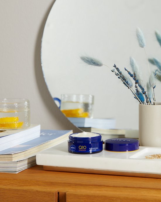 Nivea Q10 Energy nachtcrème potje op een dienblad naast boeken.