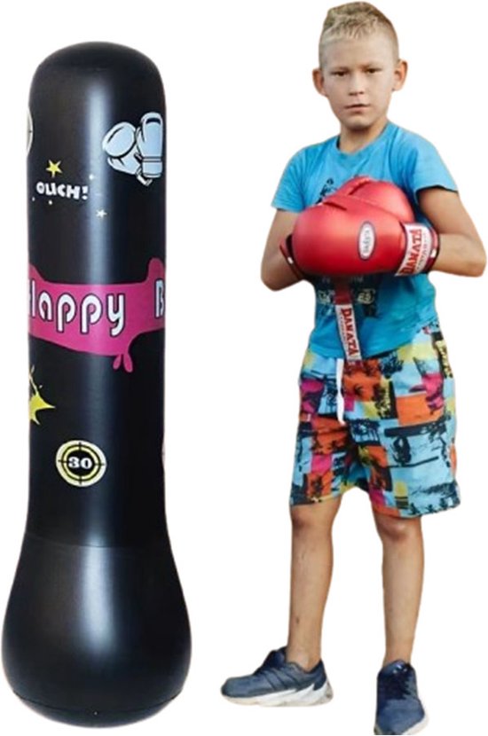 Jongen in blauw shirt en kleurrijke korte broek met rode bokshandschoenen staat naast een zwarte opblaasbare bokszak met roze 'Happy B' opdruk.