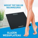 Zwarte glazen personenweegschaal met Grundig logo, naast een vrouw met blote benen.