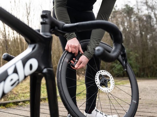 Handen gebruiken een zilveren CO2-patroon met zwarte hoes op de velg van een racefiets.