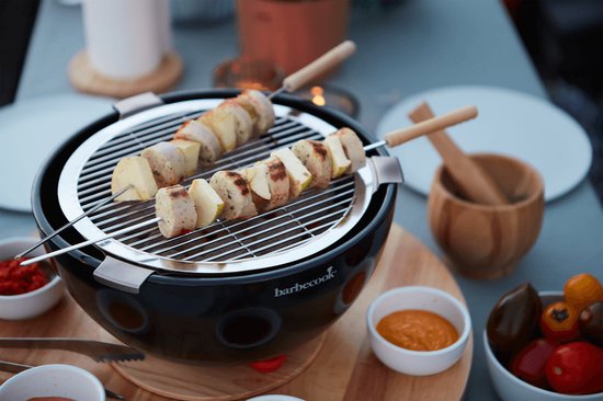 Zwarte tafelgrill met twee spiesjes met worst en stukjes appel, dichtbij.