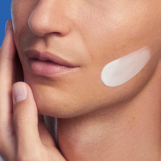 Close-up van een mannelijk gezicht met een witte crème op de wang.