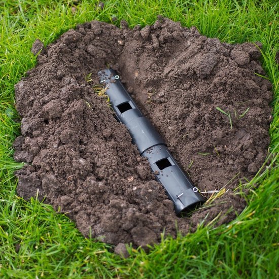 Een zwarte, diervriendelijke mollenkoker van 25 cm, deels ingegraven in gras en aarde.