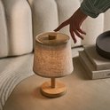 Vrouw activeert draadloze tafellamp met houten knop en linnen kap.