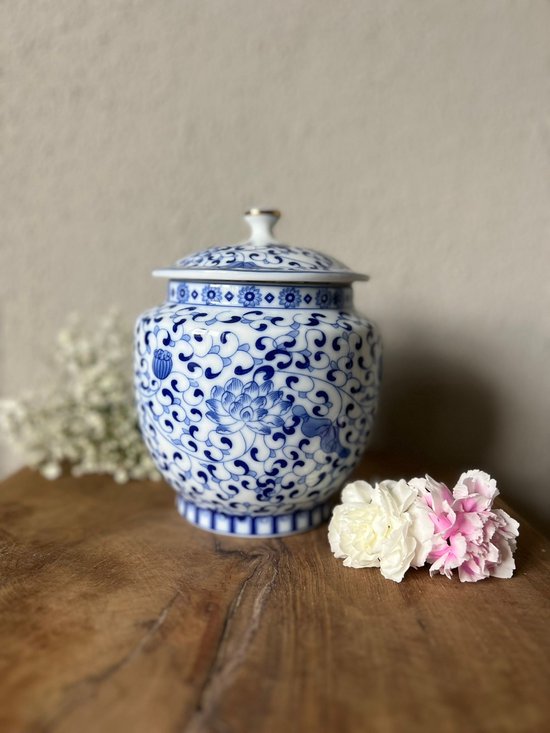 Blauw-witte porseleinen urn met gedetailleerd bloemenpatroon en deksel, op een houten tafel.