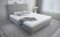 Wit matras met een grijze deken en kussens erop, op een bed in een moderne slaapkamer.