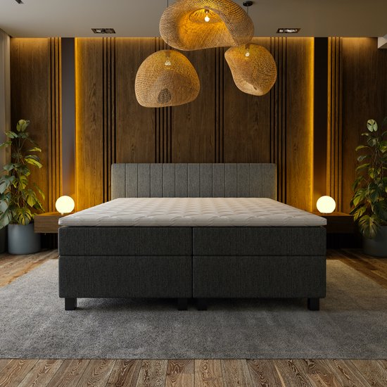 Grijze boxspring bed met wit topmatras, in een slaapkamer met houten lamellenwand en omgevingsverlichting.